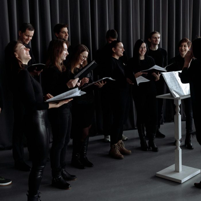 A group of men and women singing with a conductor during choir practice.